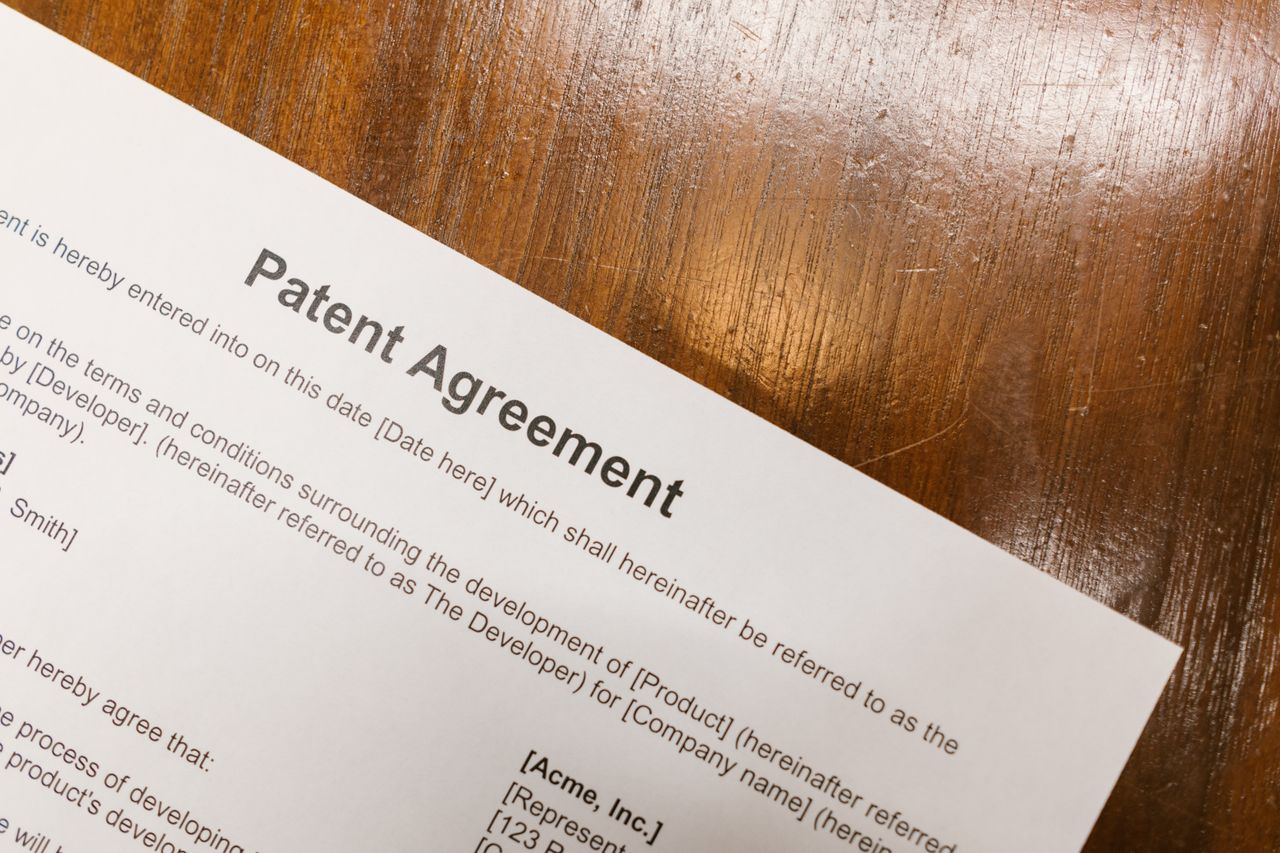 about-us-01 Detailed close-up of a patent agreement document on a polished wooden table.